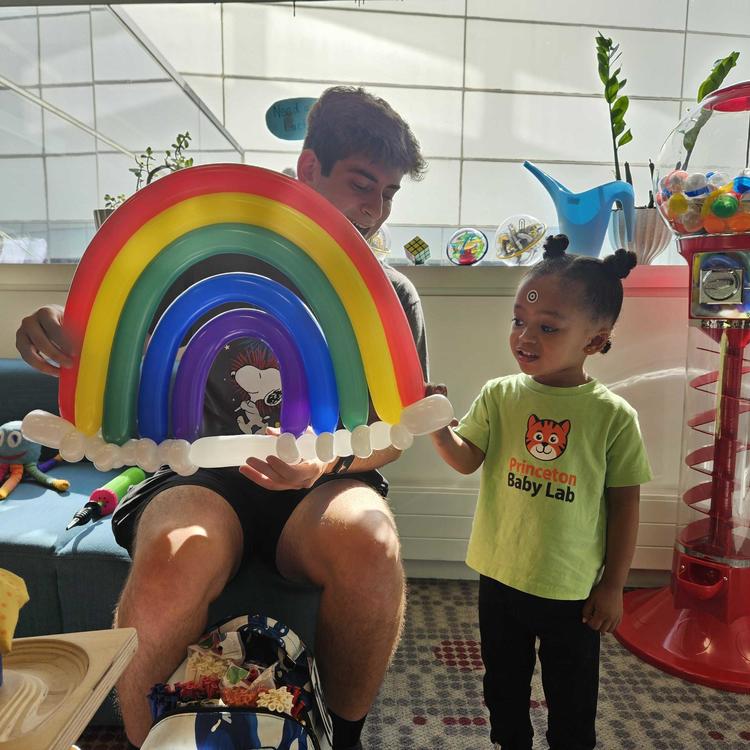 Undergrad research assistant and a child with a Baby Lab t-shirt on holding a balloon animal of a rainbow