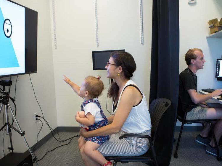 Researcher behind curtain observing child and mother engaged in activity